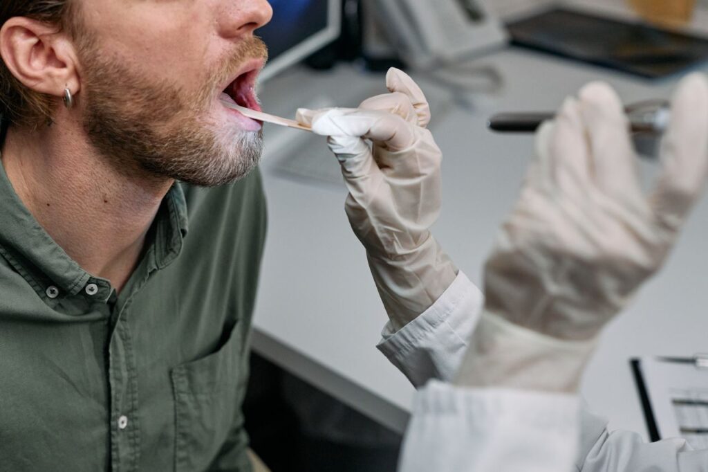 Médico examinando a garganta de um paciente com abaixador de língua em consultório