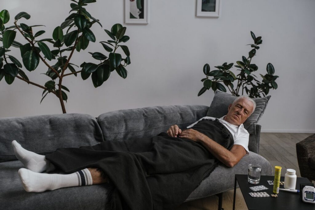 Idoso descansando no sofá em casa com medicamentos ao lado, em contexto de cuidado com a saúde no inverno